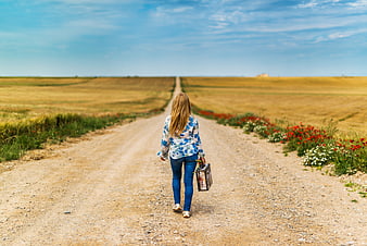 Woman walking away on dirt road with suitcase