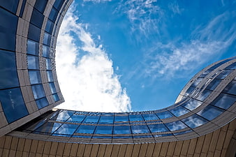 Low-angle view of modern curved glass architecture against blue sky