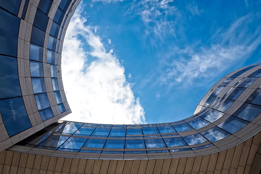 Low-angle view of modern curved glass architecture against blue sky