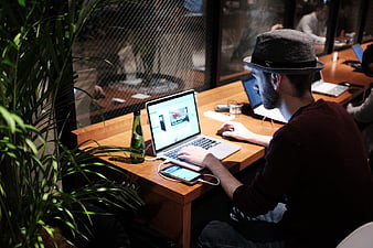 Man in Fedora Working on Laptop at Wooden Desk