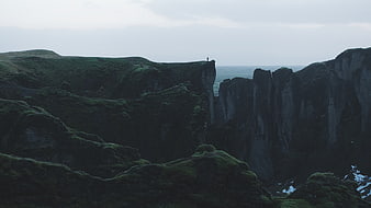 Lone Hiker on Dramatic Mossy Cliff Edge Overlooking Ocean