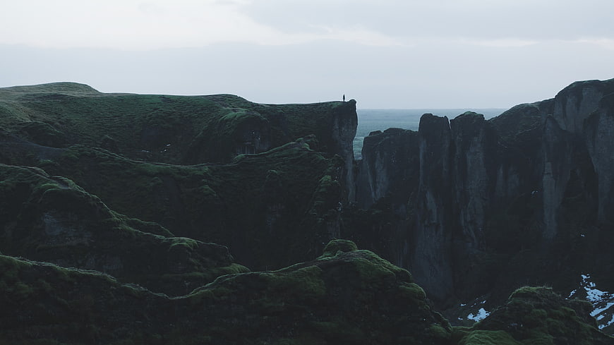 Lone Hiker on Dramatic Mossy Cliff Edge Overlooking Ocean