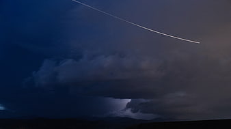 Dramatic airplane contrail cutting through dark storm clouds at dusk