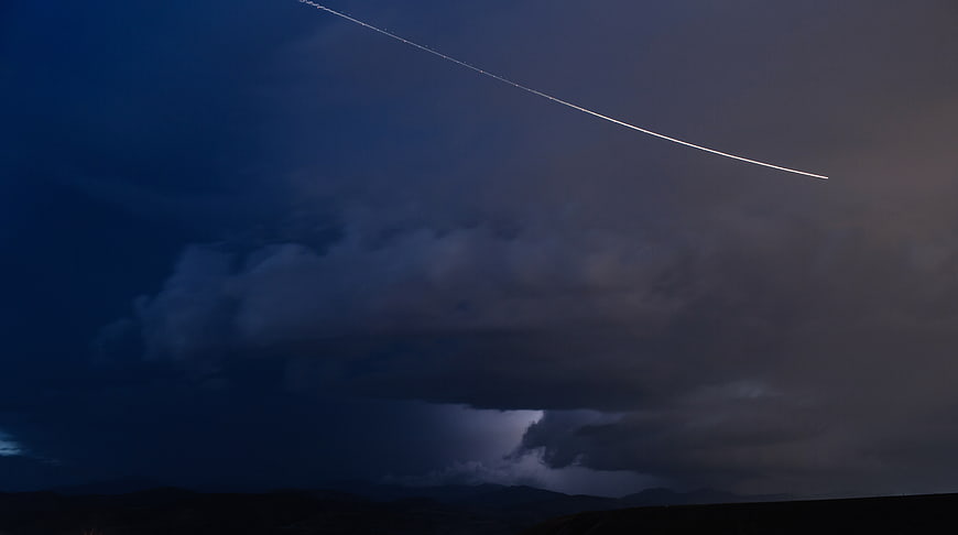 Dramatic airplane contrail cutting through dark storm clouds at dusk