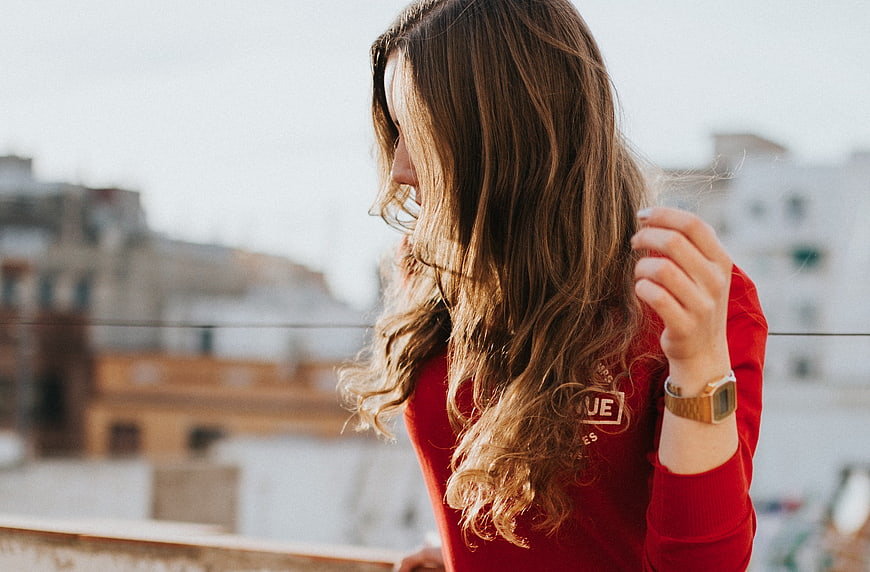Woman in Red Sweater Touching Hair on Balcony