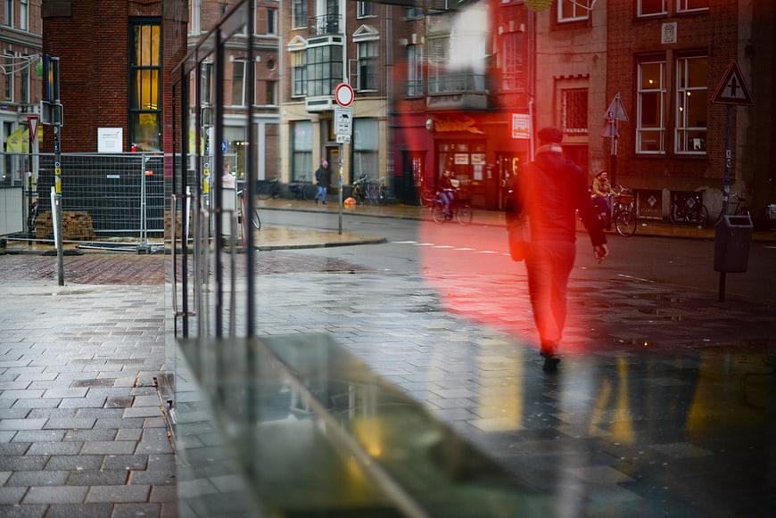 Man Walking on Wet Street Reflected in Glass Window
