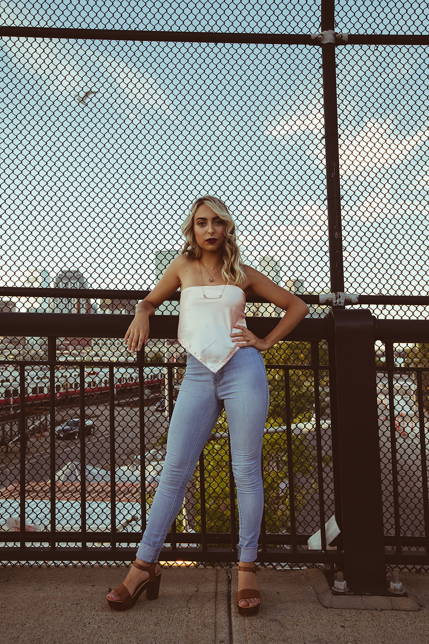 Stylish blonde woman posing on urban bridge at sunset
