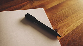 Black pen on blank notepad on wooden desk