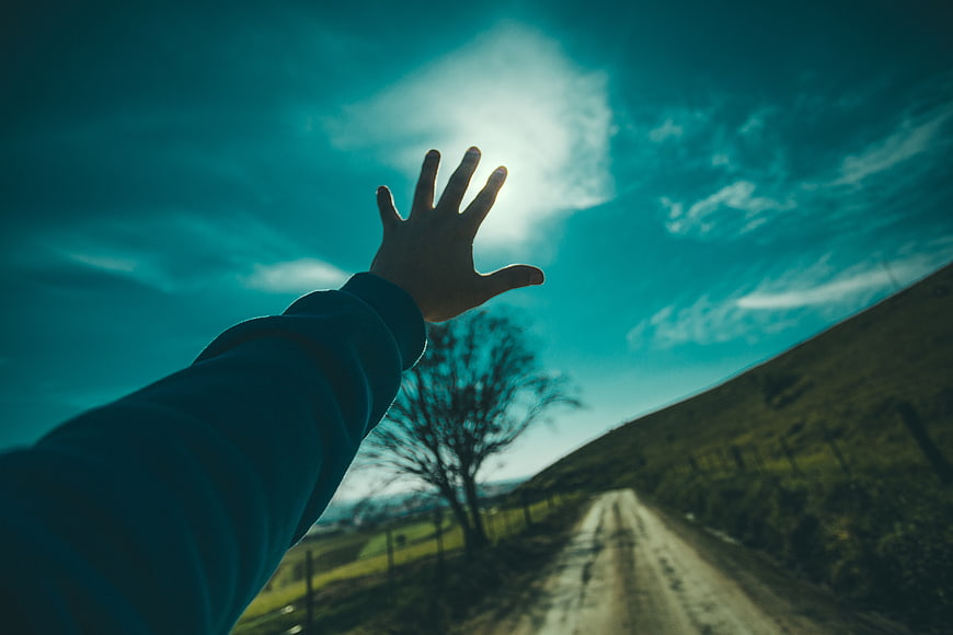 Man Reaching Hand Towards Sun On Rural Road