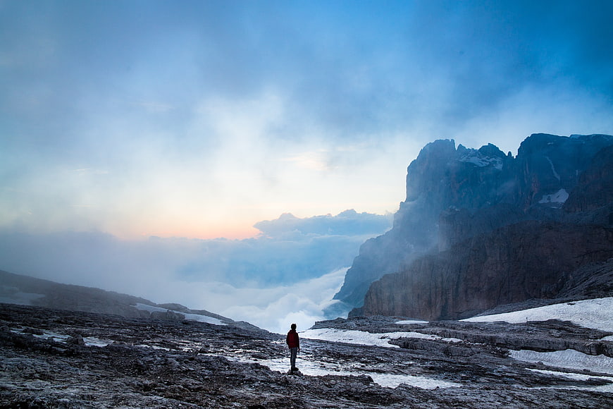 Lone Hiker Standing on Rocky Mountain Ridge Above Sea of Clouds