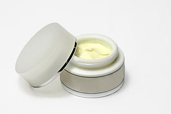 Open jar of yellow face cream with lid on white background