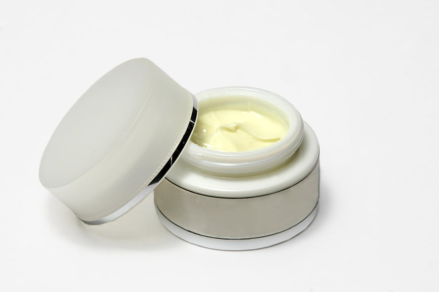 Open jar of yellow face cream with lid on white background
