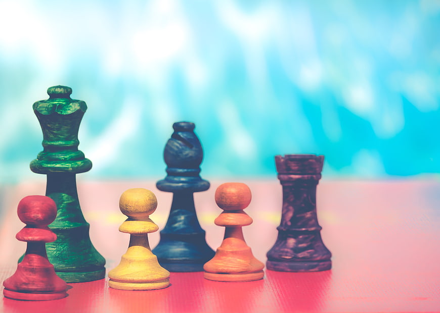 Colorful Wooden Chess Pieces on Pink Surface with Blue Background