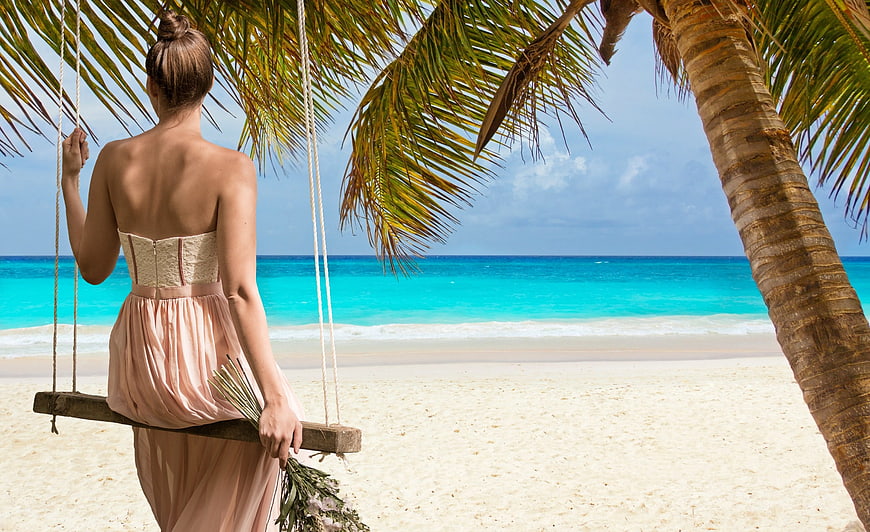 Woman in Pink Dress Sitting on Beach Swing Under Palm Tree