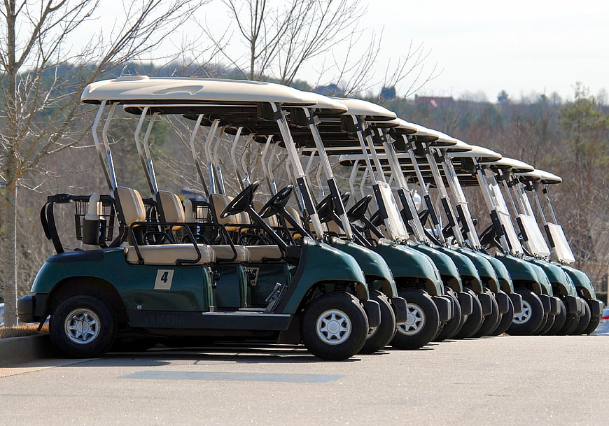Row of green golf carts parked on asphalt