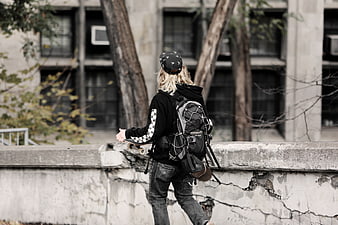 Skateboarder with Backpack Walking on Urban Concrete Wall