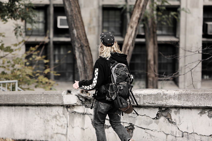Skateboarder with Backpack Walking on Urban Concrete Wall