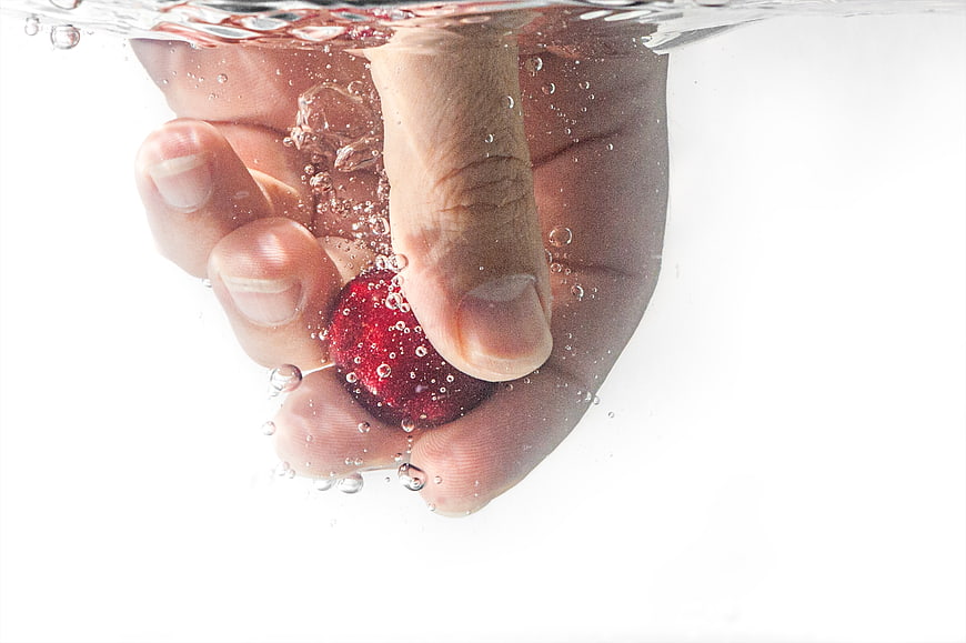 Hand holding red berry underwater with bubbles