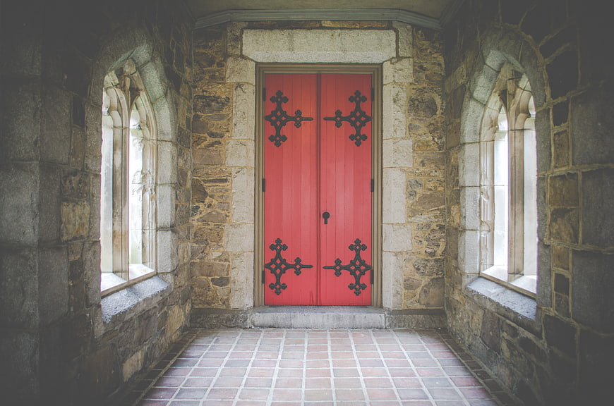 Red Gothic Door in Stone Hallway with Arched Windows