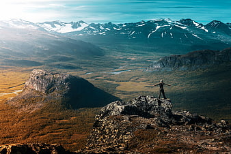 Hiker standing on rocky mountain peak overlooking vast valley