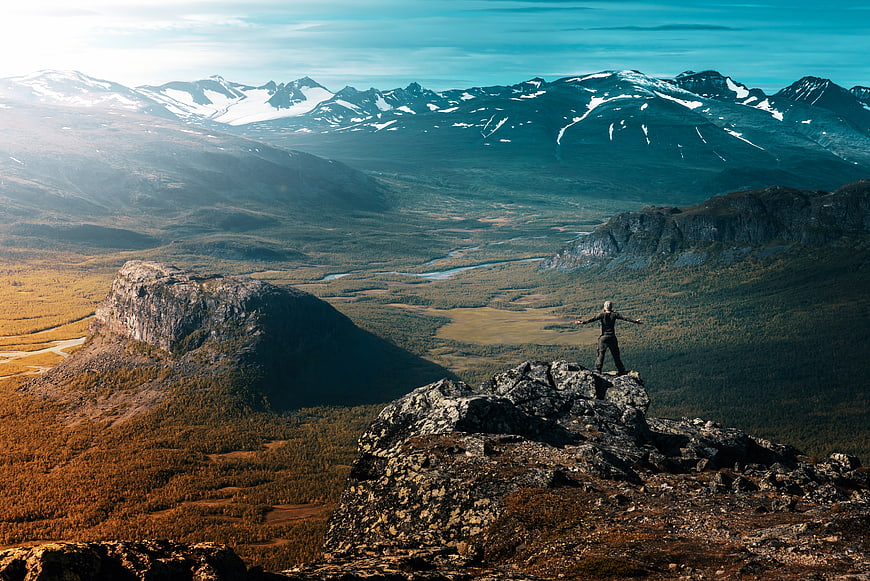 Hiker standing on rocky mountain peak overlooking vast valley