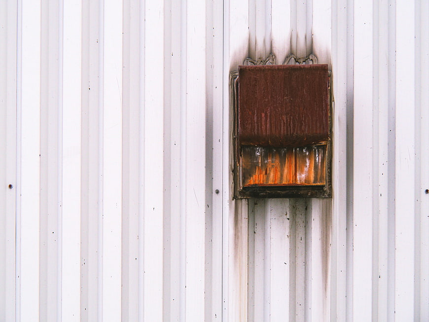 Rusty industrial vent on white corrugated metal wall