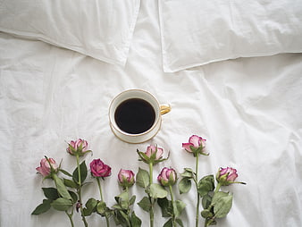 Flat lay of coffee cup and pink roses on white bed