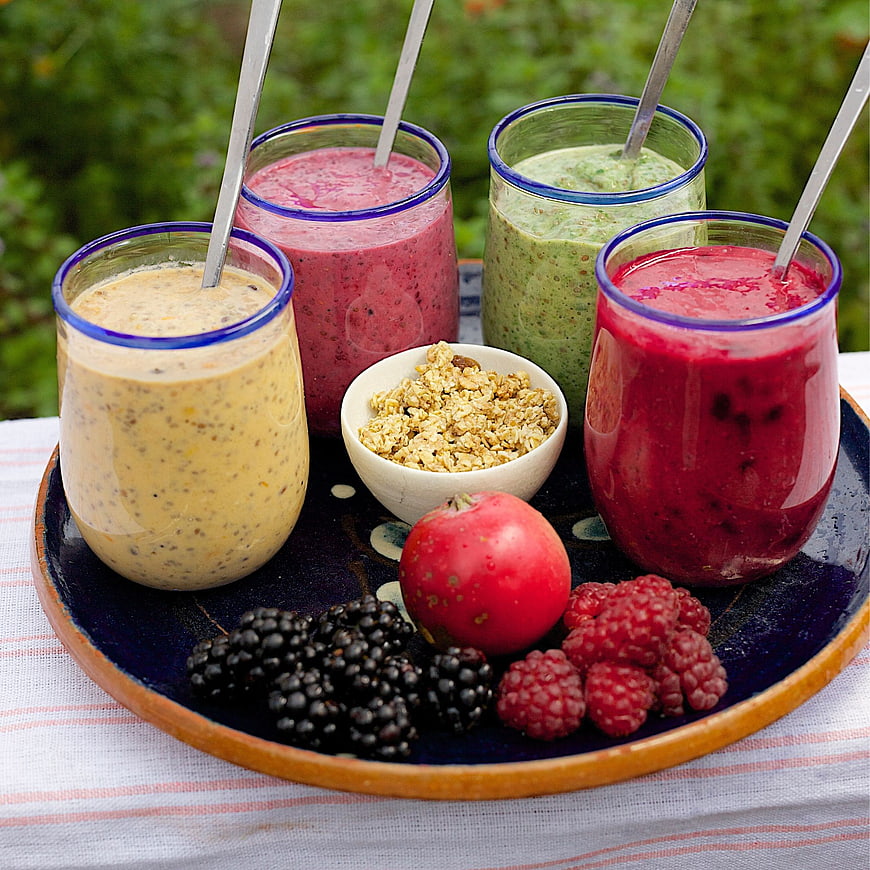 Colorful fruit smoothies with fresh berries and granola on a tray