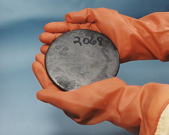 Gloved hands holding a dark circular metal disc marked 2068