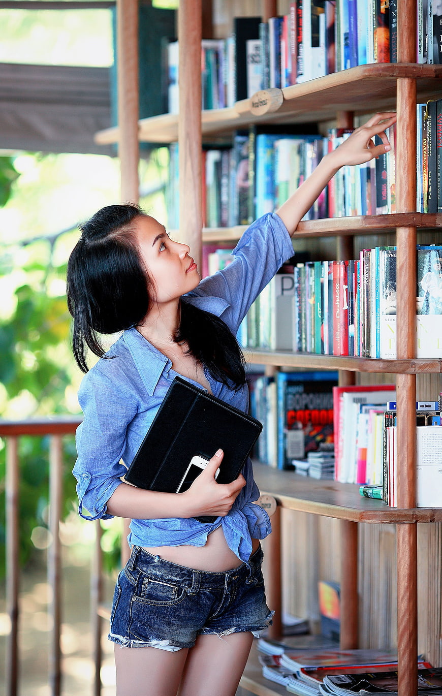 Young woman reaching for book on wooden shelf