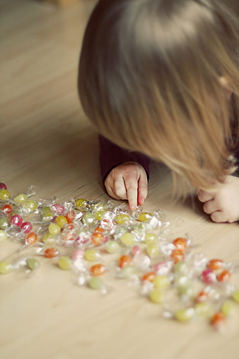 Toddler Girl Reaching for Colorful Wrapped Candies on Floor
