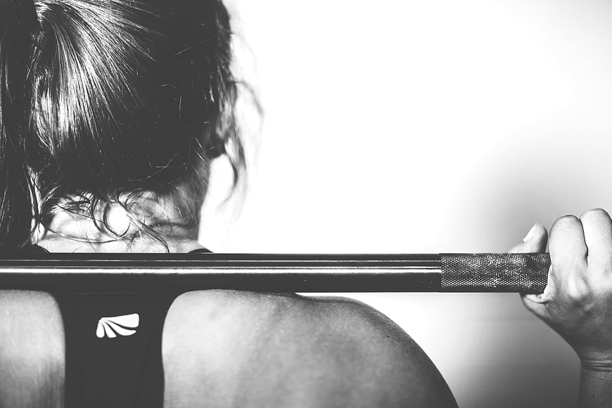 Woman lifting barbell from behind in black and white