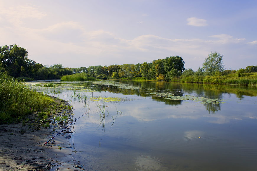 Fishing rod on riverbank with calm water and trees