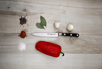 Flat lay of red bell pepper, spices, and knife on wood