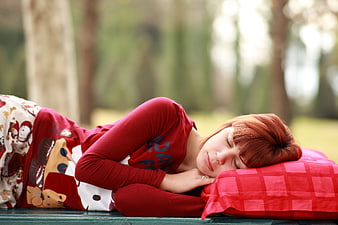 Young woman sleeping on park bench with red pillow