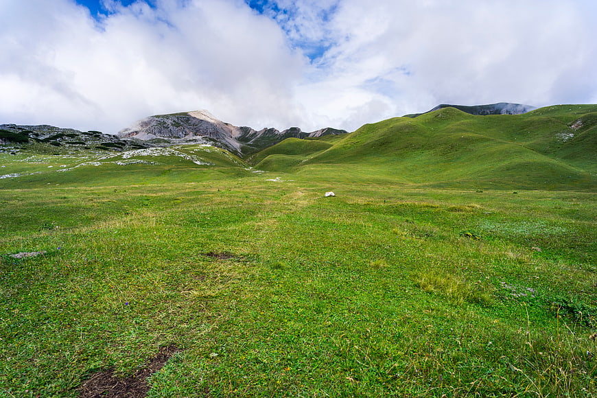 Lush Green Mountain Meadow with Rolling Hills and Cloudy Sky