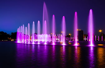 Illuminated purple fountain jets reflecting on water at night