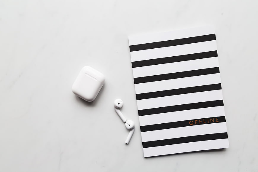 Minimalist flat lay of wireless earbuds and striped notebook