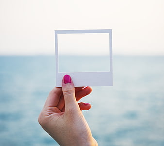 Hand holding white paper frame against blurred ocean background