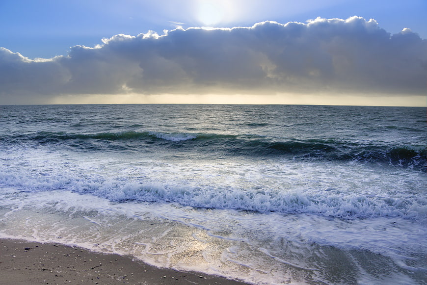 Ocean Waves Crashing on Sandy Beach Under Cloudy Sky