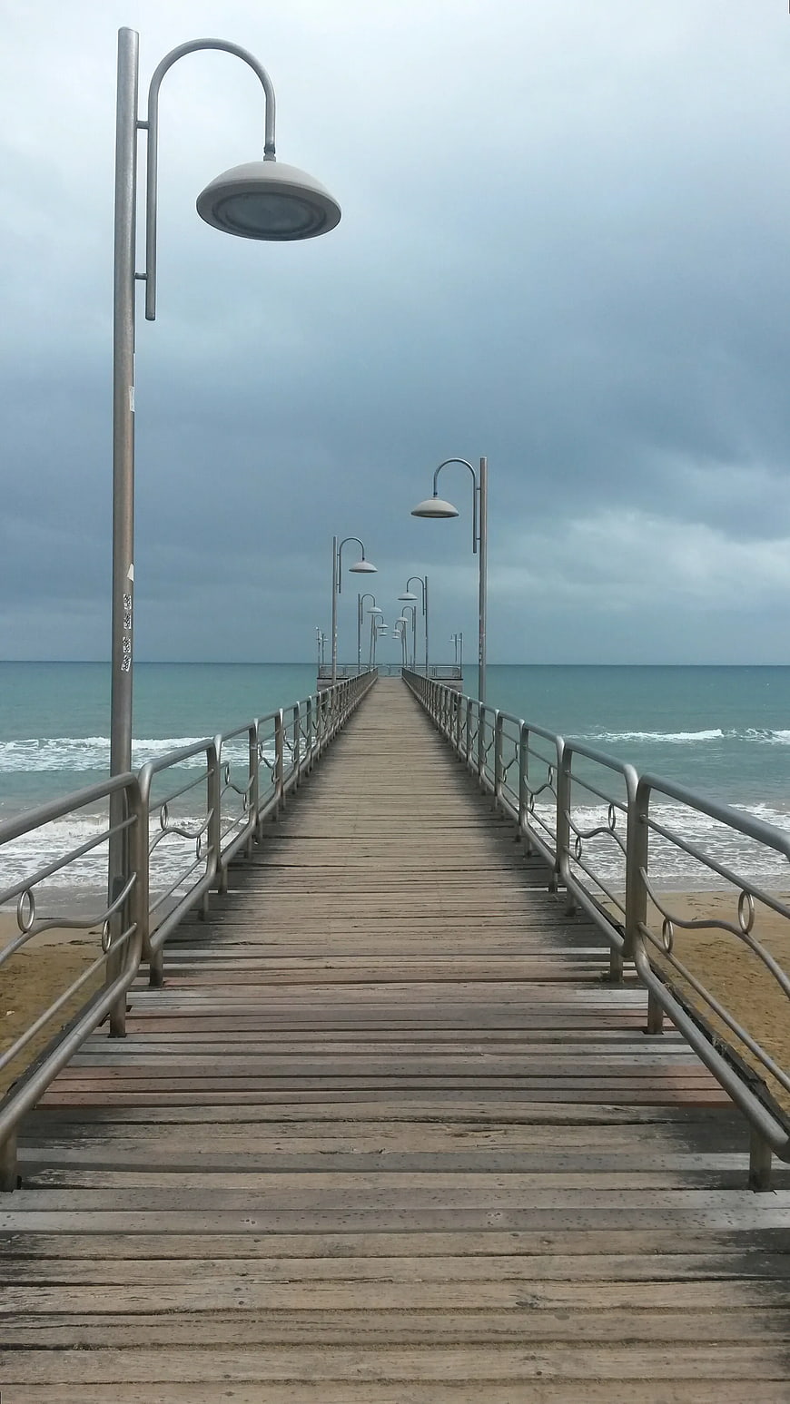 Wooden pier extending into ocean under cloudy sky