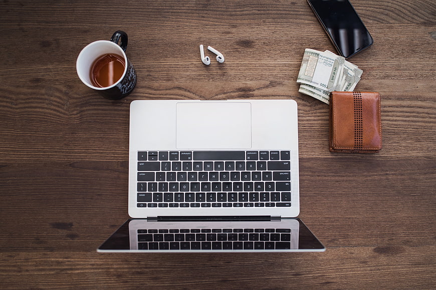 Flat lay of laptop, coffee, wallet, and cash on wooden desk