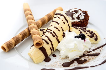 Healthy banana dessert with chocolate sauce, whipped cream, and wafer rolls
