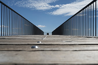 Low angle view of wooden bridge deck with metal railings and blue sky