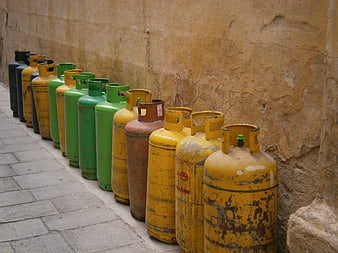 Row of weathered yellow and green gas cylinders against a textured stone wall