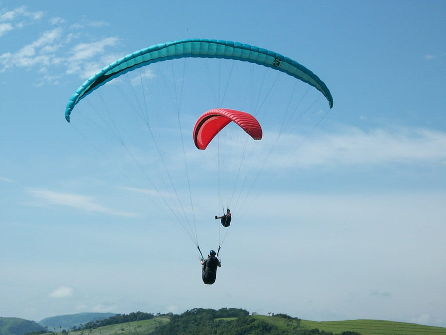 Two paragliders flying over green hills under blue sky