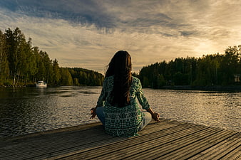 Woman meditating on wooden dock at sunset
