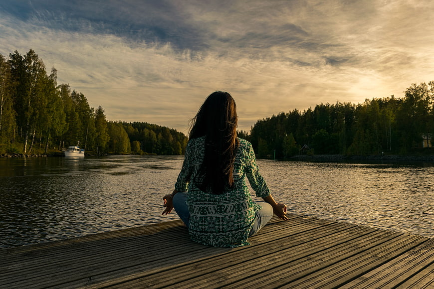 Woman meditating on wooden dock at sunset