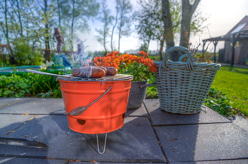 Miniature orange bucket grill with sausages in a sunny garden