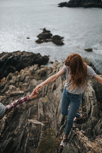 Couple holding hands hiking on rocky coastal cliff